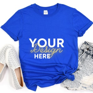 May include: A royal blue t-shirt with the text "YOUR Design HERE" in white and yellow lettering. The t-shirt is laid flat on a white surface with a pair of white canvas shoes and denim shorts.