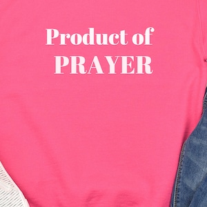 May include: A pink sweatshirt with the text "Product of PRAYER" in white lettering.