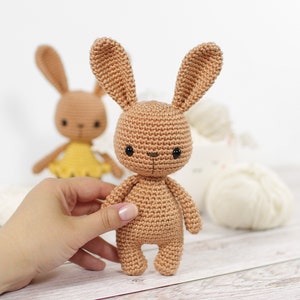 Small crocheted amigurumi bunny, standing in front of a yarn bowl and balls of yarn