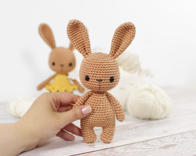 Small crocheted amigurumi bunny, standing in front of a yarn bowl and balls of yarn