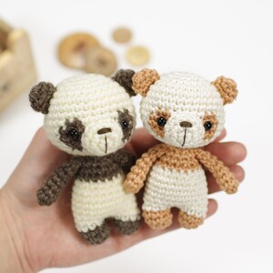 May include: Two crocheted panda bears, one with brown and white fur and the other with brown, white, and tan fur. The bears are holding hands and have black eyes and noses.