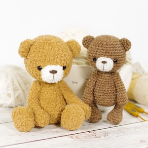 May include: Two crocheted teddy bears, one brown and one beige, sitting on a white surface with yarn balls in the background.