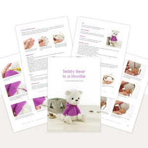 K&ouml;nnte beinhalten: Ein H&auml;kelmusterbuch mit dem Titel "Teddy Bear in a Hoodie" mit Anleitungsseiten. Das Buch zeigt einen wei&szlig;en geh&auml;kelten Teddyb&auml;ren mit einem lila Kapuzenpullover. Die Seiten zeigen Schritt-f&uuml;r-Schritt-Anleitungen mit Bildern. Der Hintergrund ist wei&szlig;.