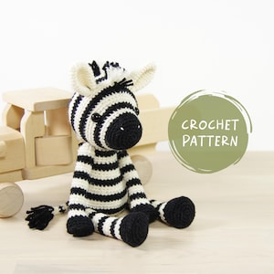 May include: Crochet pattern for a black and white striped zebra amigurumi toy. The zebra is sitting on a wooden toy truck.