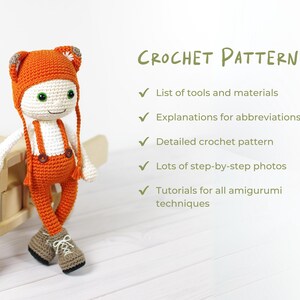 May include: A crocheted amigurumi doll wearing orange overalls and a matching hat. The doll is standing on a wooden toy airplane. The image includes the text "CROCHET PATTERN" and a list of features included in the pattern.