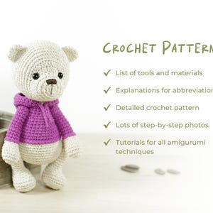 K&ouml;nnte beinhalten: Geh&auml;kelter Teddyb&auml;r in Hellbeige mit einem lila Kapuzenpullover. Das Bild enth&auml;lt den Text "CROCHET PATTERN" und listet Funktionen wie "Liste der Werkzeuge und Materialien" und "Detailliertes H&auml;kelmuster" auf. Der B&auml;r hat eine braune Nase und schwarze Augen.