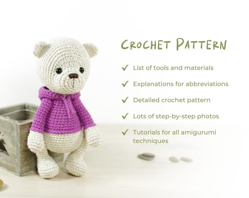 K&ouml;nnte beinhalten: Geh&auml;kelter Teddyb&auml;r in Hellbeige mit einem lila Kapuzenpullover. Das Bild enth&auml;lt den Text "CROCHET PATTERN" und listet Funktionen wie "Liste der Werkzeuge und Materialien" und "Detailliertes H&auml;kelmuster" auf. Der B&auml;r hat eine braune Nase und schwarze Augen.