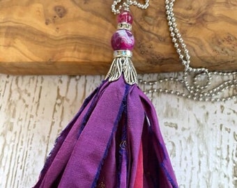 May include: A purple and red silk tassel necklace with a silver bead and chain.