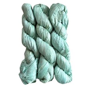May include: A bundle of light mint green silk ribbon yarn featuring a textured, crinkled appearance. The material is wound into a series of interconnected loops, displaying a soft, matte finish with visible frayed edges along the length of the fabric.