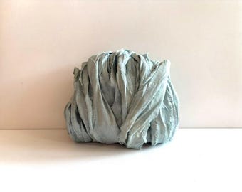 May include: A bundle of light blue ribbon with a soft, matte texture and frayed, raw edges. The fabric is gathered into a rounded, voluminous shape, showcasing the delicate, uneven weave of the material and its consistent pale blue color throughout.
