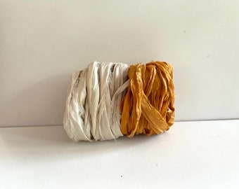 Könnte beinhalten: Zwei Spulen mit Seidenband, eine weiße und eine senfgelb. Das Band ist zerknittert und hat einen rustikalen, handgefertigten Look.
