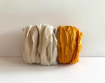 May include: A bundle of fabric ribbon featuring two distinct sections. The left portion consists of multiple layers of cream-colored, frayed-edge textile strips, while the right portion is a solid, vibrant mustard yellow fabric strip.