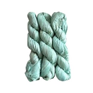 May include: A close-up of a thick, braided rope in a soft, muted teal color. The rope is tightly woven, with visible texture and a slightly wrinkled appearance. The rope is likely made of fabric or a similar material.