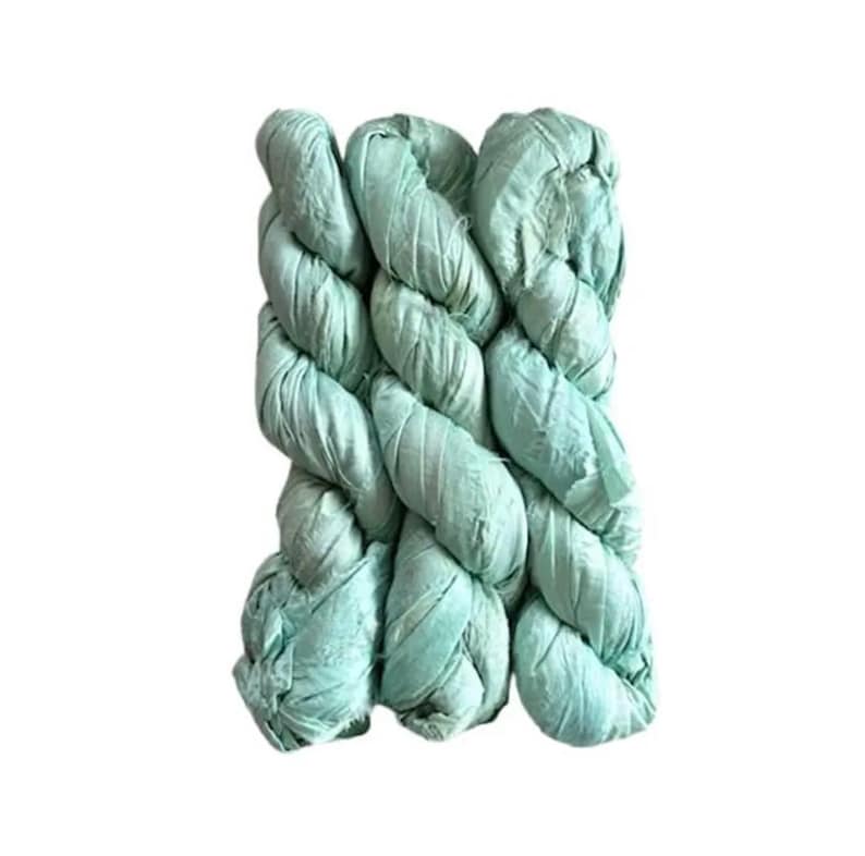 May include: A close-up of a thick, braided rope in a soft, muted teal color. The rope is tightly woven, with visible texture and a slightly wrinkled appearance. The rope is likely made of fabric or a similar material.