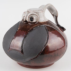 Może przedstawiać: Dzbanek ceramiczny w kolorze brązowym i czarnym z białą pokrywką i uchwytem w kształcie sowy. Dzbanek ma unikalny, abstrakcyjny wzór.