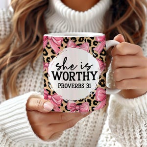 Peut inclure: Mug en c&eacute;ramique blanche avec l'inscription "she is WORTHY PROVERBS 31" en noir. Le mug pr&eacute;sente un fond &agrave; imprim&eacute; l&eacute;opard avec des n&oelig;uds roses. Un objet d&eacute;coratif.