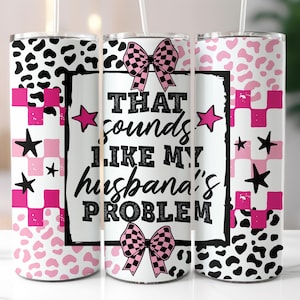 May include: A white tumbler with a black and pink design. The tumbler features the text "THAT sounds LIKE MY husband's PROBLEM" with pink stars and checkered bows. The design includes pink and black leopard print and checkered patterns.