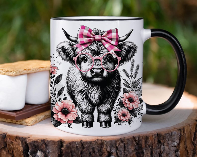Peut inclure: Une tasse en c&eacute;ramique blanche avec une anse noire. La tasse pr&eacute;sente une illustration en noir et blanc d'une vache des Highlands portant des lunettes roses et un n&oelig;ud en vichy rose et blanc. La vache est entour&eacute;e de fleurs roses et de feuilles vertes.