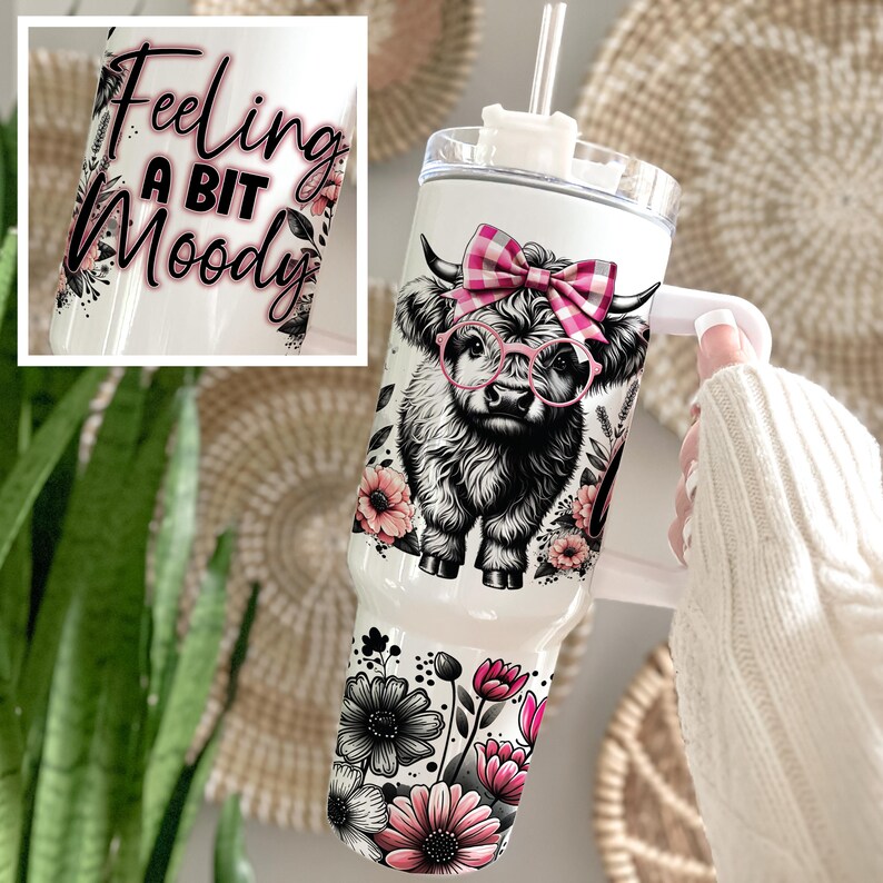May include: White stainless steel tumbler with a black and white Highland cow wearing pink glasses and a pink and white gingham bow. The tumbler has a black handle and a pink floral design. The text "Feeling a bit Moody" is printed on the tumbler.