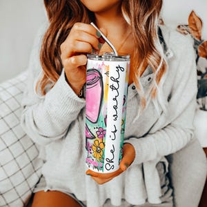 May include: A stainless steel tumbler with a colorful floral and jar design. The tumbler has the text "She is worthy" in a vertical stripe. The tumbler includes a silver straw.