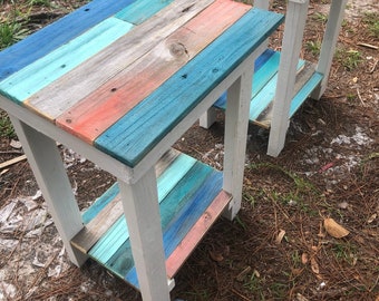 May include: Two small wooden end tables with a white painted frame and a multi-colored top and shelf. The top and shelf are painted in shades of blue, teal, and pink.