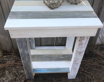 May include: A white, blue, and gray wooden side table with a shelf. The table is made of reclaimed wood and has a distressed finish. Two glass fishing floats are on top of the table.