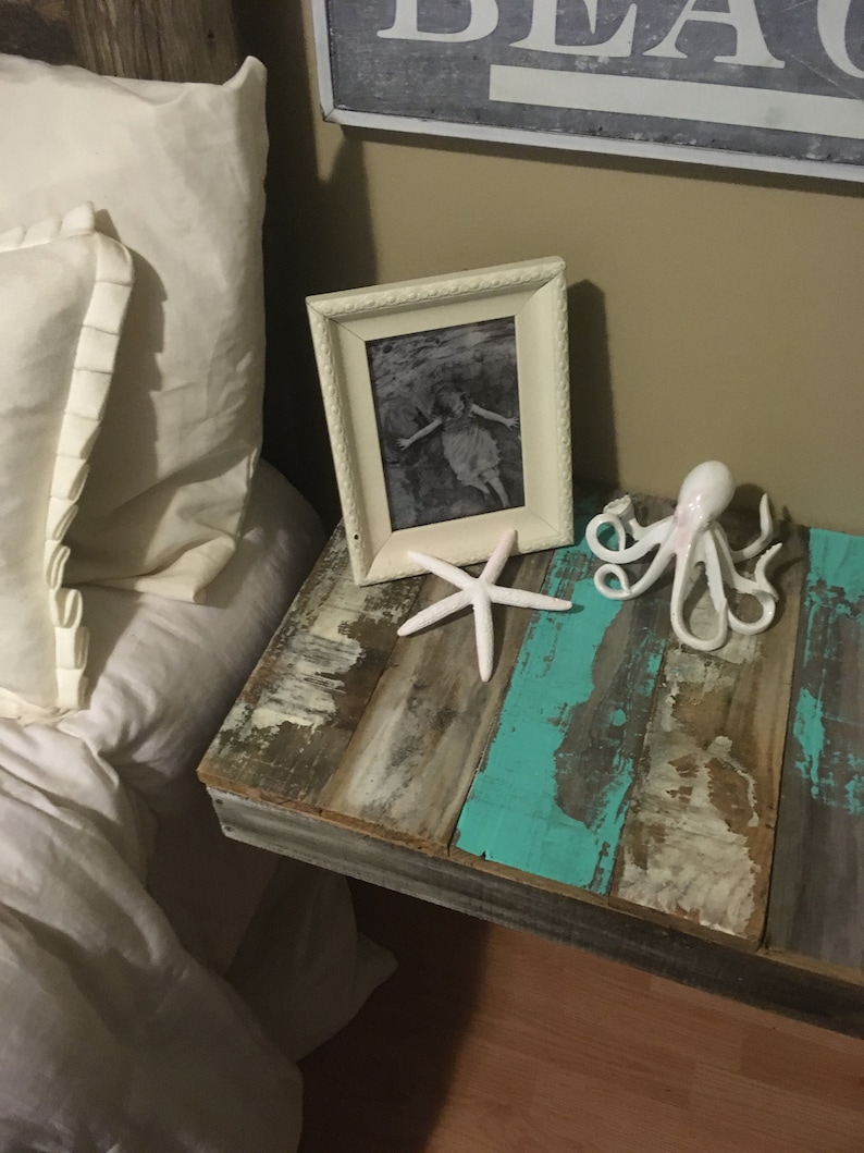 May include: A rustic wooden nightstand with a turquoise blue paint finish. The nightstand has a white picture frame with a black and white photo of a girl in a dress. There is a white starfish and a white octopus figurine on the nightstand.