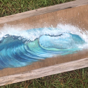 May include: A framed painting of a blue ocean wave crashing on a beach. The wave is painted in shades of blue and green, with white foam at the crest. The painting is framed in a rustic wooden frame.