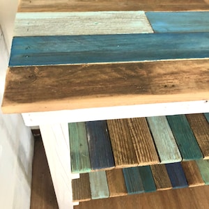 May include: A white wooden shelf unit with three shelves. The shelves are made of reclaimed wood painted in shades of blue, green, and brown.