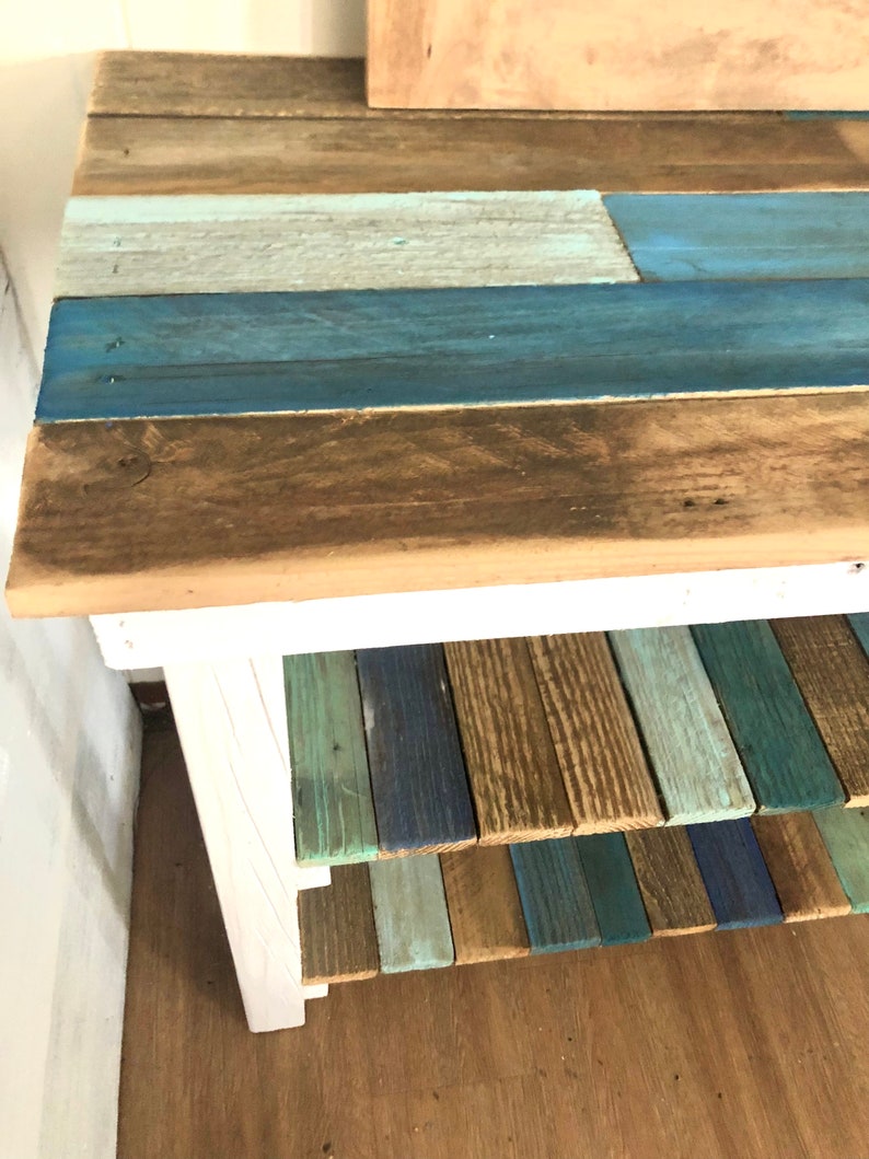 May include: A white wooden shelf unit with three shelves. The shelves are made of reclaimed wood painted in shades of blue, green, and brown.
