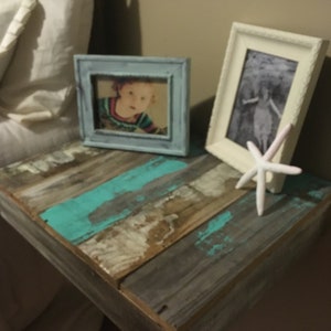 May include: A rustic wooden shelf with a turquoise and white paint finish. The shelf is mounted to a wall and has two framed photos on top. One photo is of a child, and the other is a black and white photo. A white starfish is placed on the shelf.