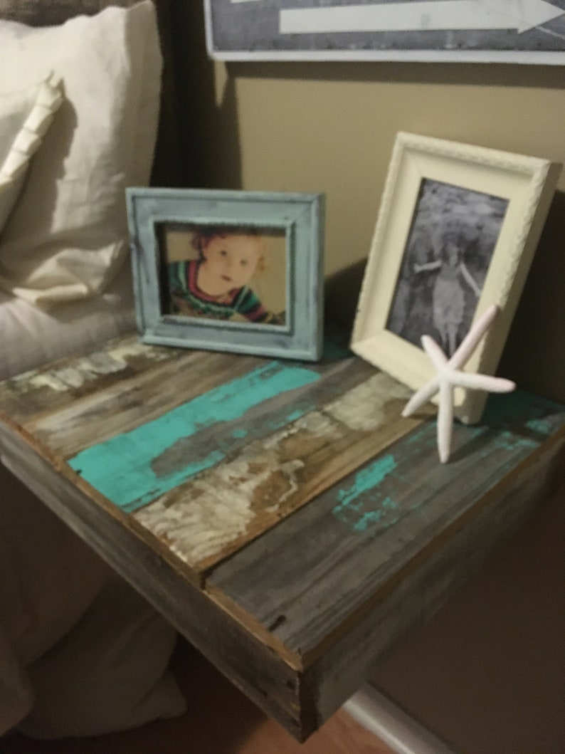 May include: A rustic wooden shelf with a turquoise and white paint finish. The shelf is mounted to a wall and has two framed photos on top. One photo is of a child, and the other is a black and white photo. A white starfish is placed on the shelf.