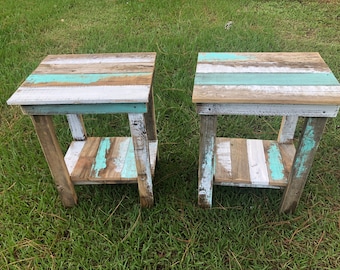 May include: Two rustic side tables made from reclaimed wood. The tables feature a square top with a shelf below, painted in shades of white, teal, and natural wood tones. The tables are set on a grassy surface.
