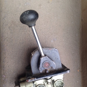 May include: A silver and black hydraulic control valve with a black rubber knob on a silver lever. The valve has multiple ports and a filter screen.