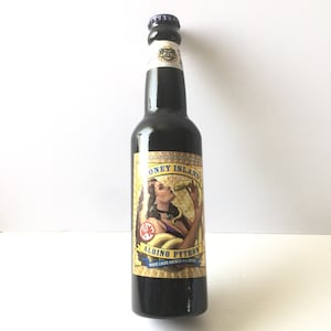May include: A brown glass bottle of Honey Island Brewing Company's Albino Python White Lager brewed with spices. The label features a woman with a snake wrapped around her neck and the text "Albino Python" in a yellow banner.