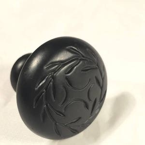 May include: Black cabinet knob with a decorative leaf design.