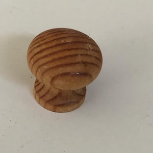 May include: A wooden cabinet knob with a rounded top and a short, cylindrical base. The knob is made of light brown wood with visible grain patterns, and it is set against a white background. This hardware is suitable for drawers and cabinets.