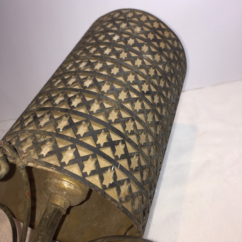 K&ouml;nnte beinhalten: Ein Lampenschirm aus Messing mit einem sternf&ouml;rmigen Ausschnittmuster. Der Lampenschirm ist aus Metall und hat eine patinierte Oberfl&auml;che.