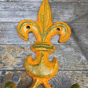 May include: Orange and green cast iron double hook with a fleur-de-lis design.