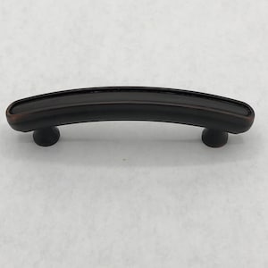 May include: A curved, black, bronze-finished cabinet pull with rounded ends.