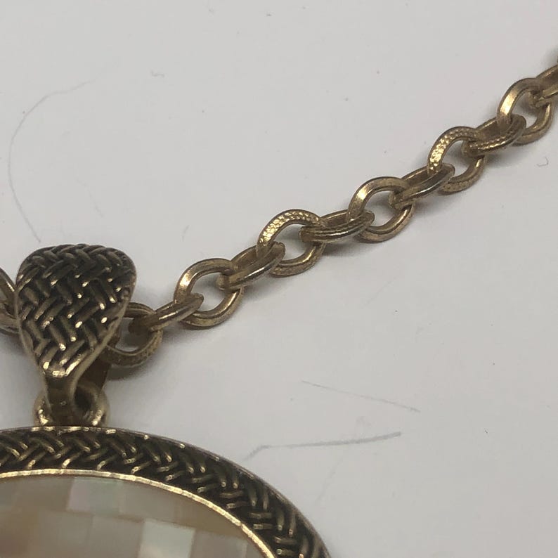 May include: A gold chain necklace with a round pendant featuring a white mother-of-pearl inlay.