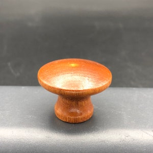 May include: A wooden knob with a rounded top and a cylindrical base. The knob is a light brown color.