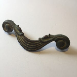 May include: A vintage, ornate, metal drawer pull with a scroll design. The pull is a dark green color with a slightly aged patina.