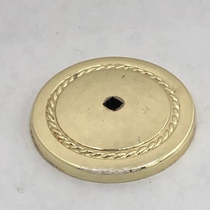 May include: A gold-colored round metal base with a rope-like design around the edge. The base has a small hole in the center.
