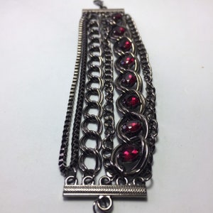 May include: A multi-strand bracelet with a black metal chain and red gemstone accents.