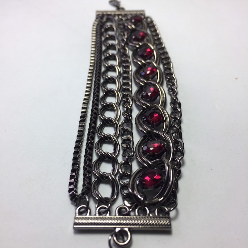 May include: A multi-strand bracelet with a black metal chain and red gemstone accents.