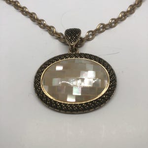May include: A gold chain necklace with an oval pendant featuring a white mother-of-pearl inlay.