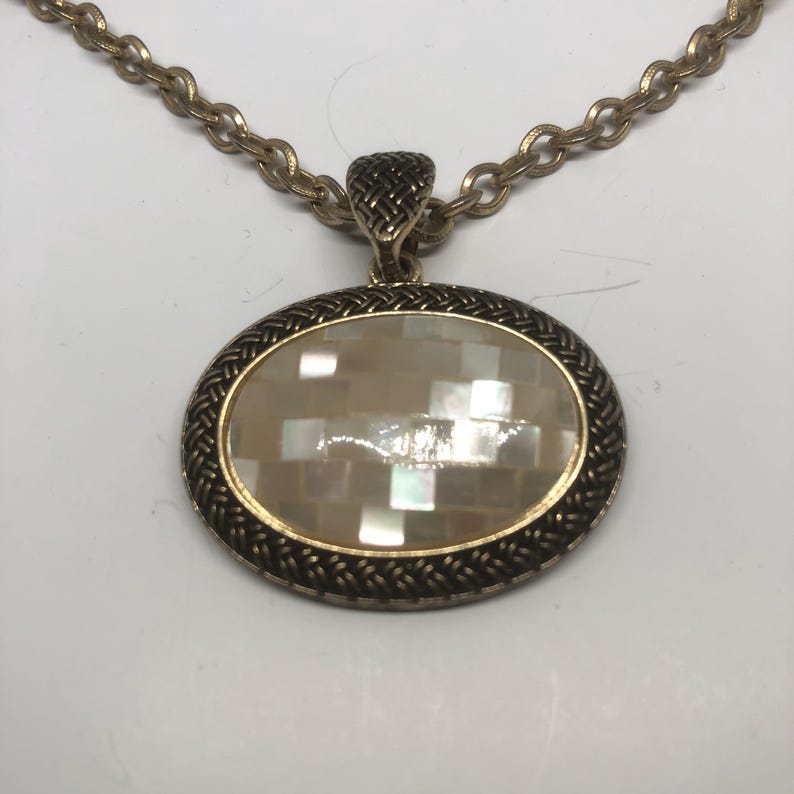 May include: A gold chain necklace with an oval pendant featuring a white mother-of-pearl inlay.