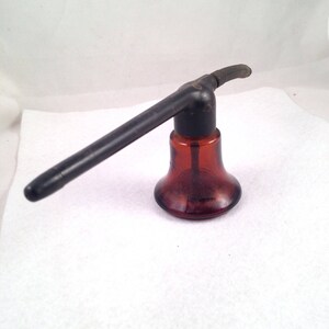 May include: A brown glass bottle with a black plastic nozzle. The bottle has a bell-shaped base and a long, thin spout.