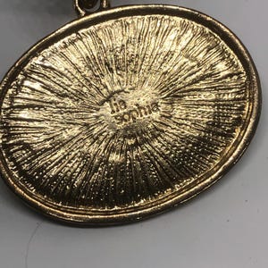 May include: Gold-toned oval pendant with a textured surface and the inscription "Tia Sophia" on the back.